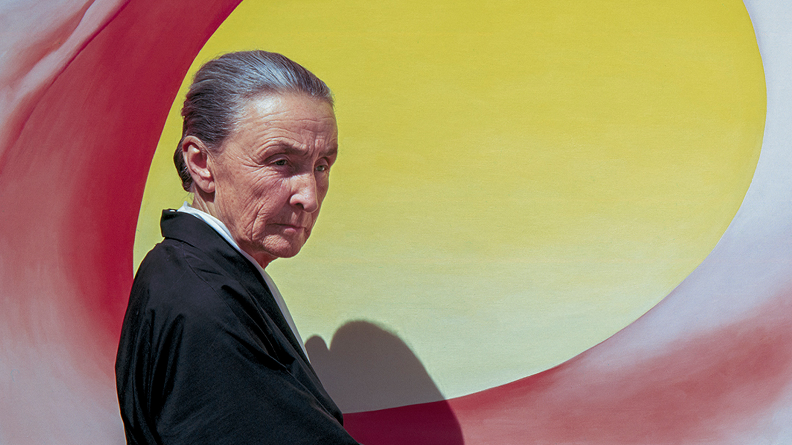Photo of artist Georgia O'Keeffe stood in front of a bright yellow painting