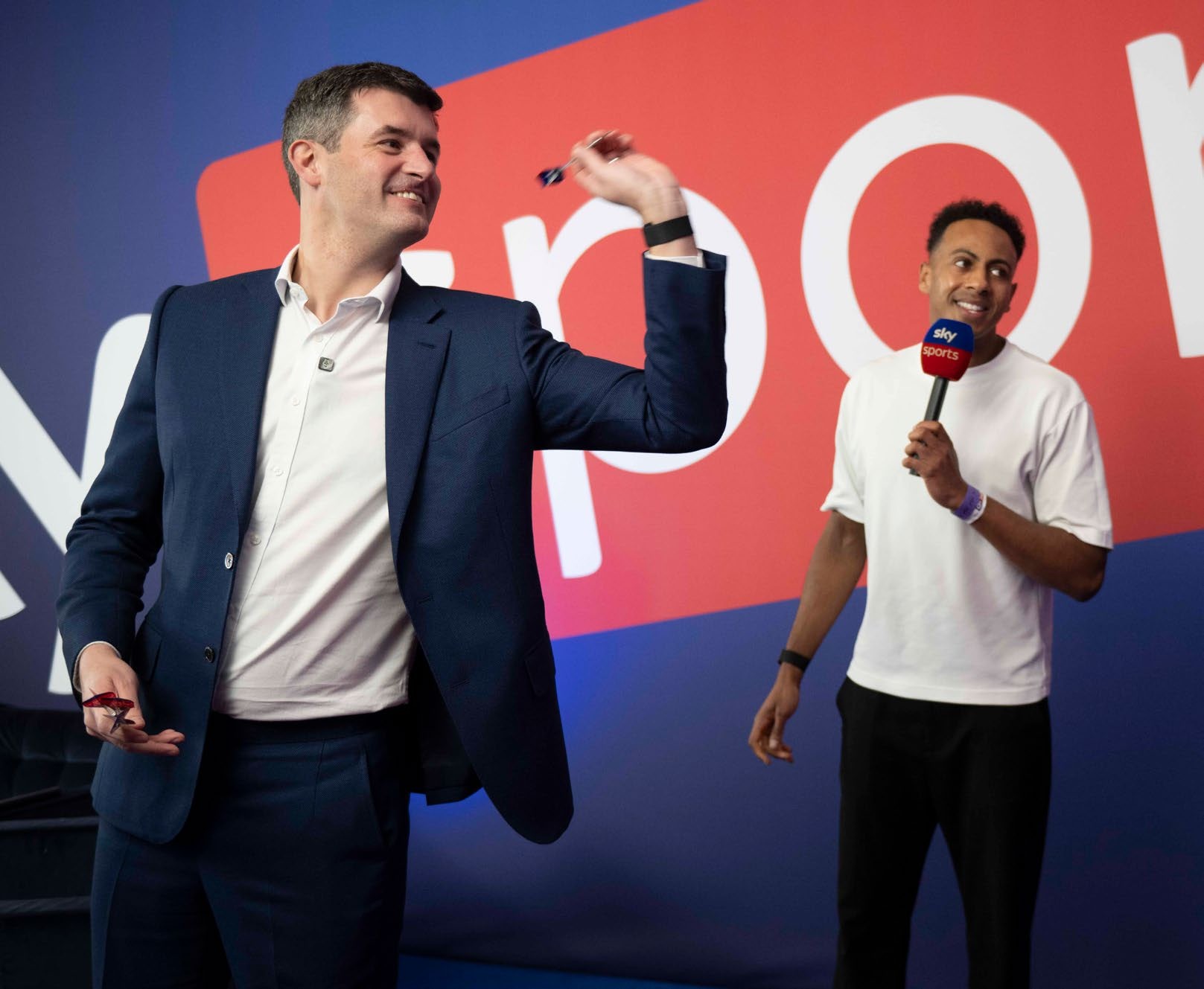 Matt Porter throws darts at a dart board with SkySports presenter Kyle Walker in the background
