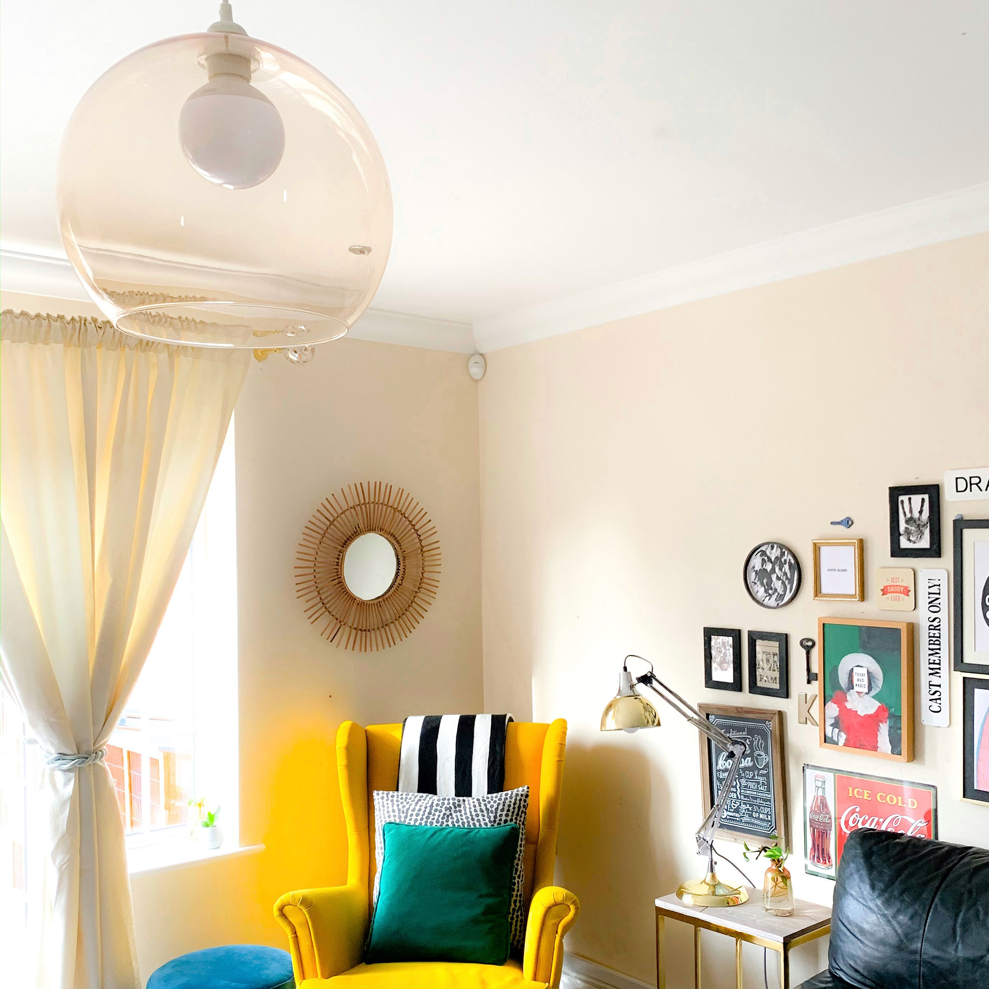 Neutral living room with yellow armchair, rattan mirror, gallery wall and glass pendant light fitting