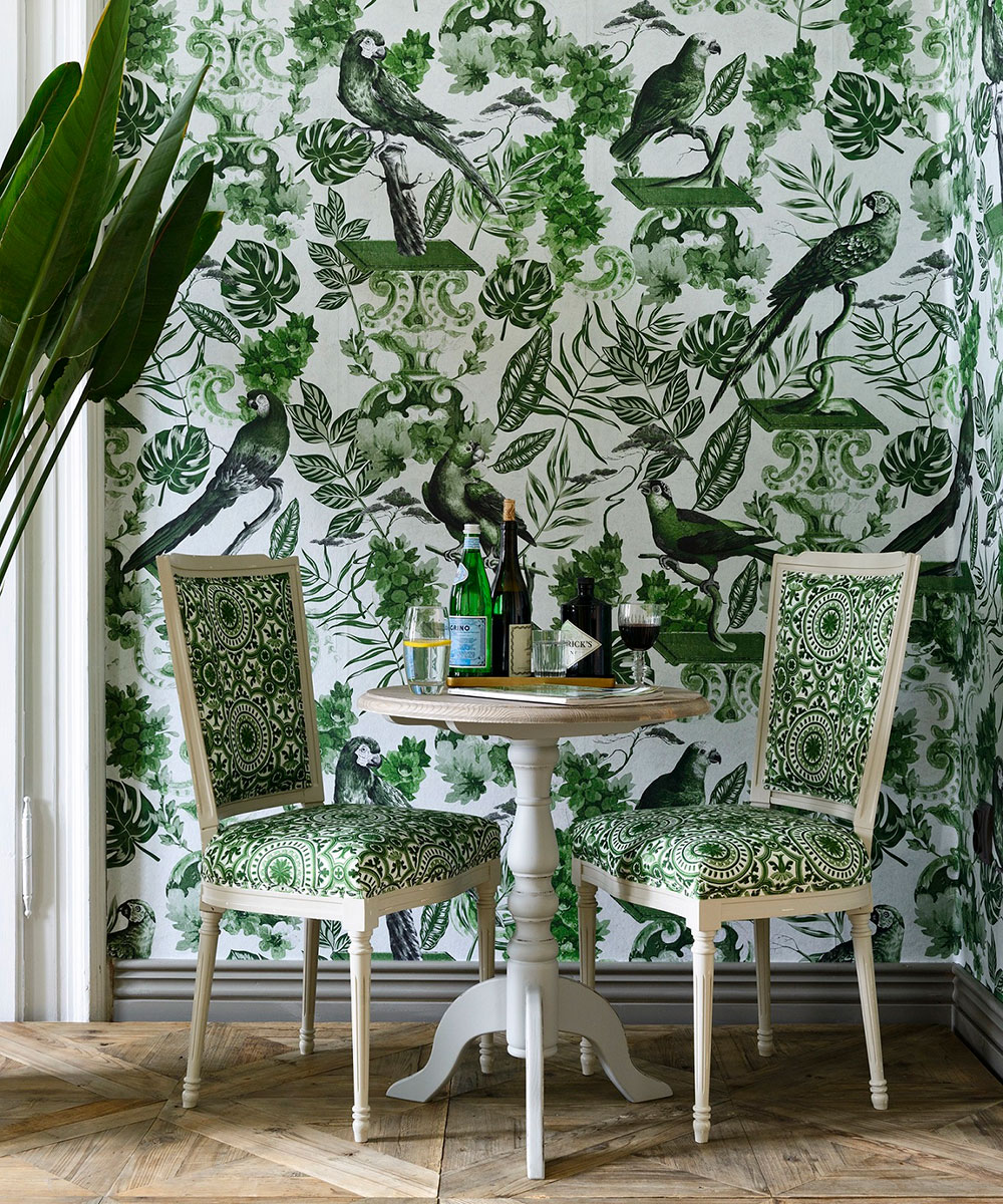 An example of wallpaper trends showing green and white plant print wallpaper behind a two seater dining table with upholstered chairs