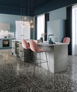 A kitchen with blue wall decor and curtains, Terrazzo flooring, pink bar stools, ten Edison-style ceiling pendant lights and grey concrete island