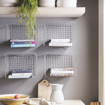 Stone kitchen worktop and shelf with white crockery, baskets attached to the grey wall with books.