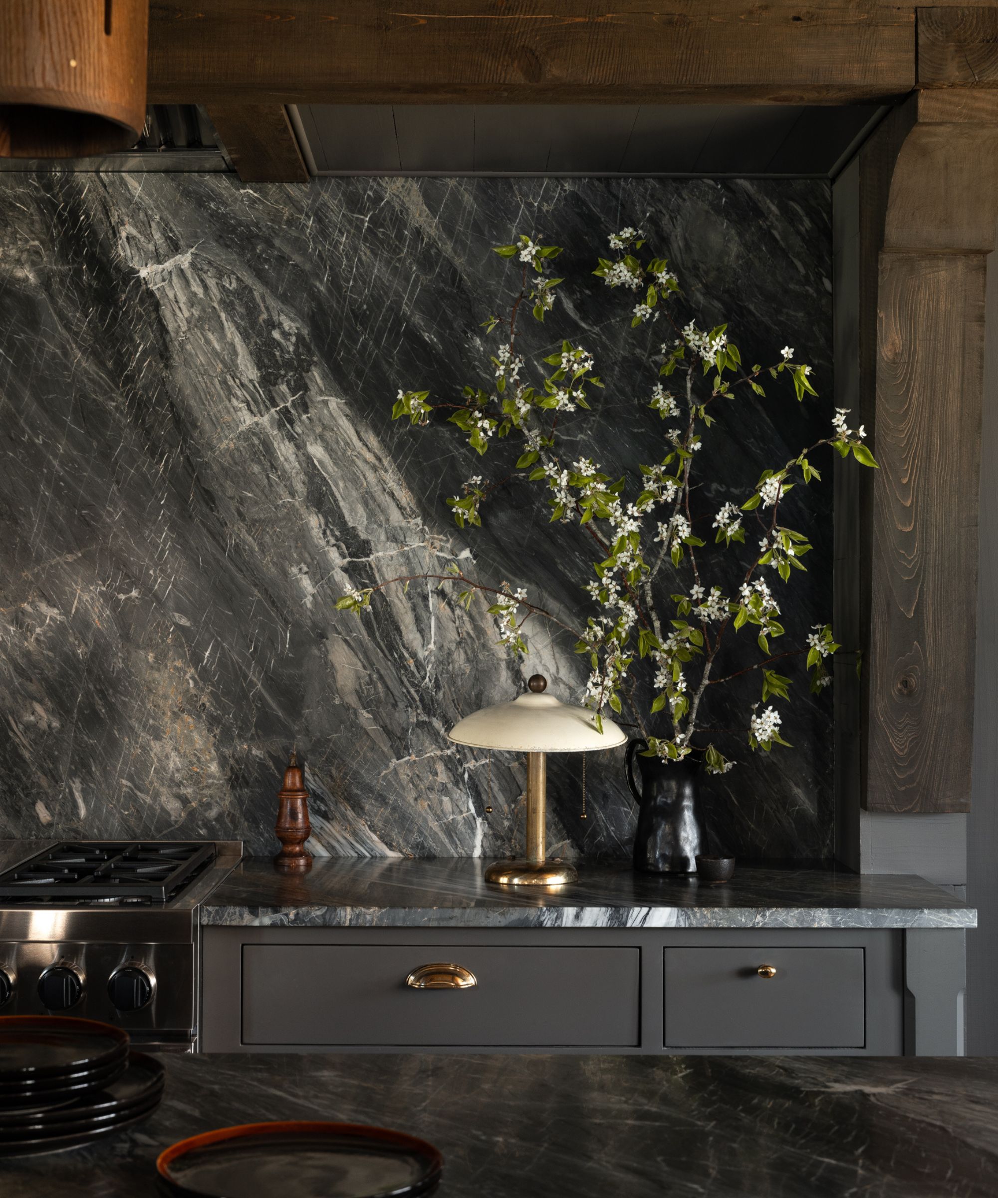 Dramatic black marble backsplash with bold veining behind a cooker in a modern farmhouse kitchen with wood beams.
