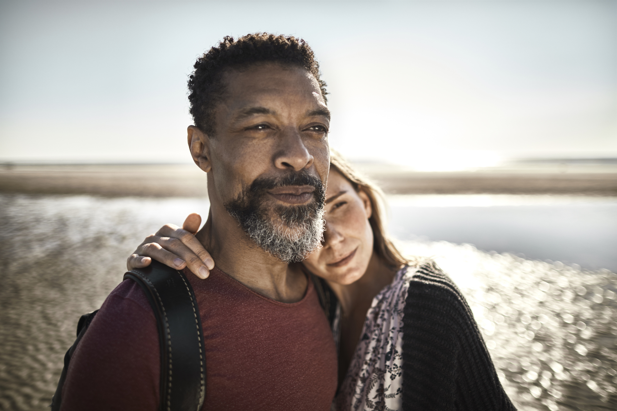 A mature couple on a beach stare off.