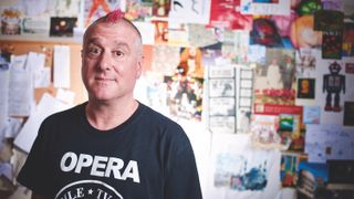 Bruce Lawson wearing an Opera t-shirt standing in front of a notice board covered with images, sketches and notes.