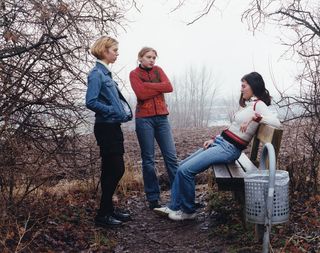 Three females in a foggy cold forest and bench