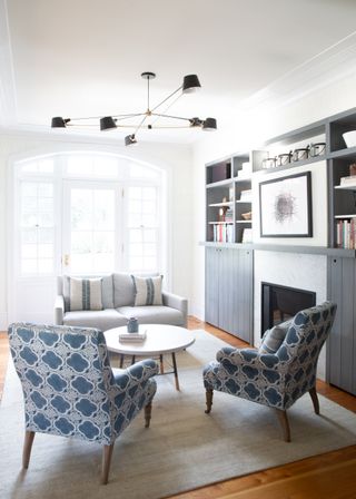 blue and white living room with hidden tv, pendant, blue couch, matching armchairs, round coffee table, bookcases