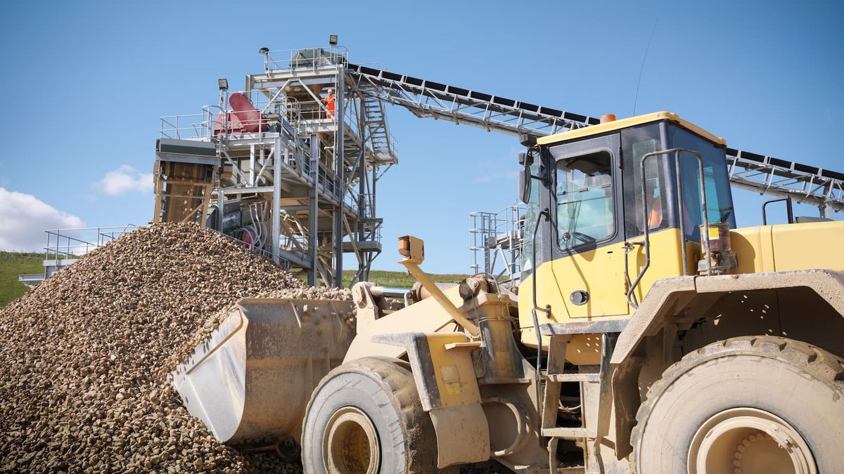 Digger picking up crushed stones from pile in quarry