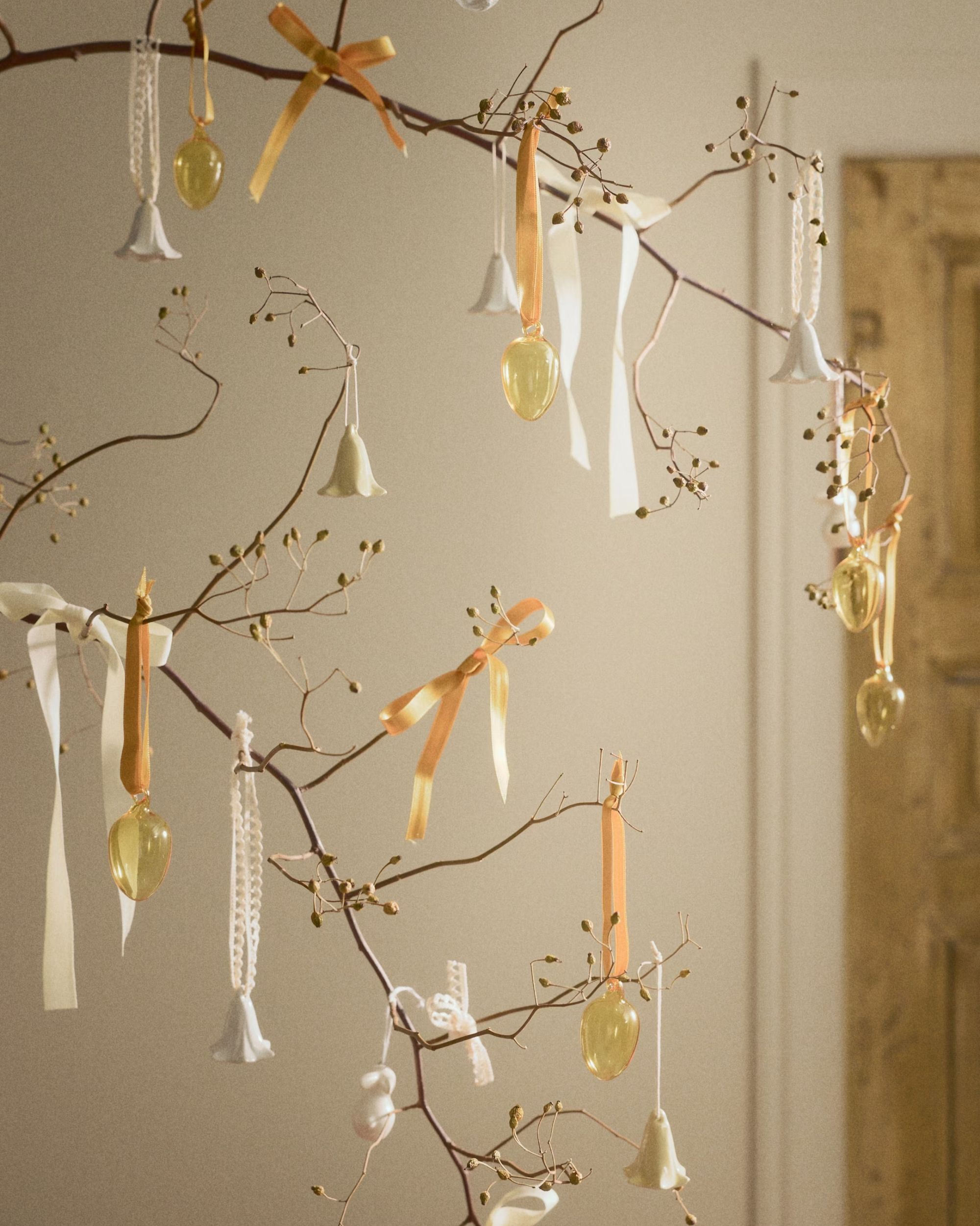 Twigs and stems adorned with orange and cream ribbons and glass egg and tulip ornaments.
