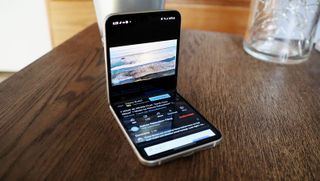 En Samsung Galaxy Z Flip 3 liggner halvt öppnad på ett träfärgad skrivbord.