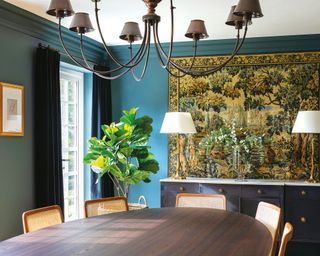 Blue dining room with antique tapestry, dark wood dining table, vase of flowers, chandlier