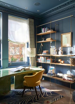 Dark blue home office with open shelving, patterned rug and yellow chair
