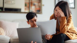 image depicts a stressed asian couple looking at pieces of paper and a laptop