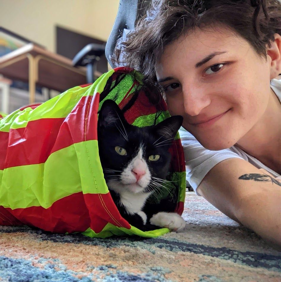 Alisa lying down next to her cat who is sitting inside of a toy tunnel