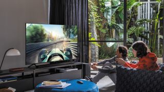 En mand og en kvinde sidder i en stue og spiller på et Samsung Q70T 4K QLED TV