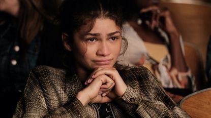 a woman (zendaya as rue) sits on a bed while holding a phone, in 'euphoria' season 2