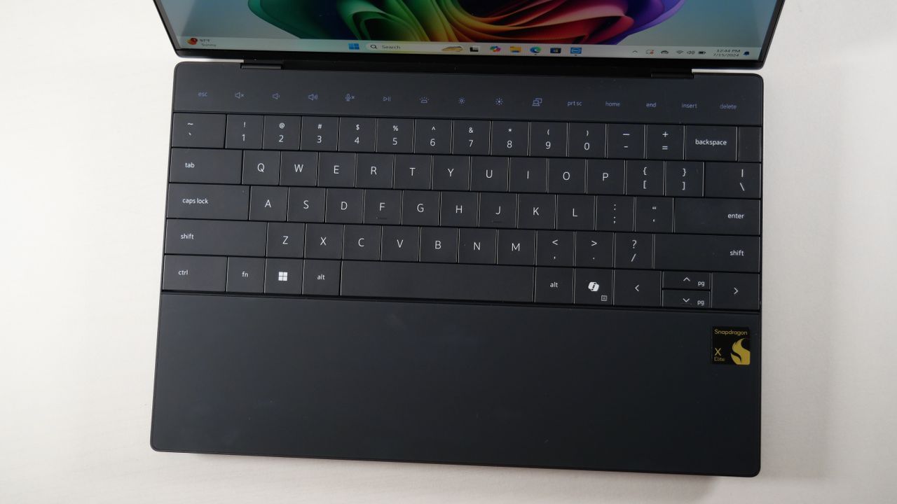 Dell XPS 13 9345 (Snapdragon X Elite) open on a white desk showing the keyboard and touchpad.