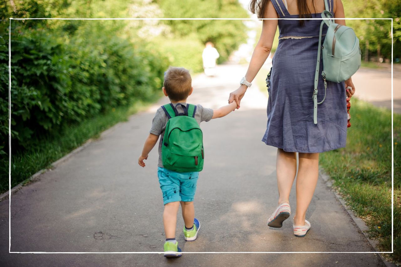 Mother holding hands with child as they walk down a path on a summer&#039;s day with backpacks on their backs