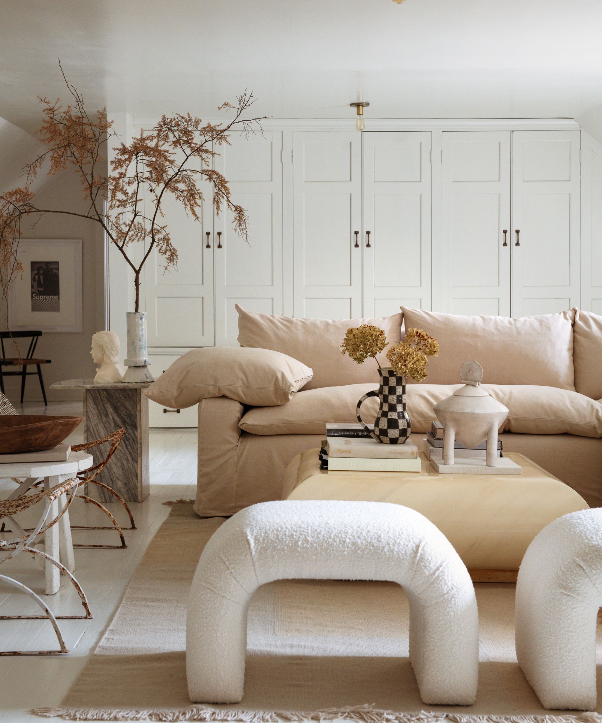 A light and airy living room with white walls and built-ins, beige sofa, pale wood coffee table, a neutral rug, and two modern boucle seats.