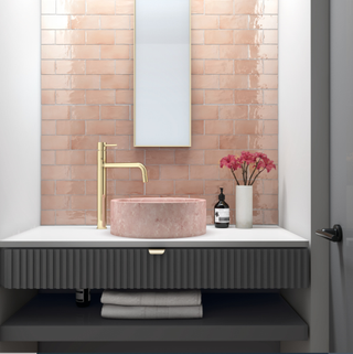 A pale pink bathroom sink and pink tiled wall