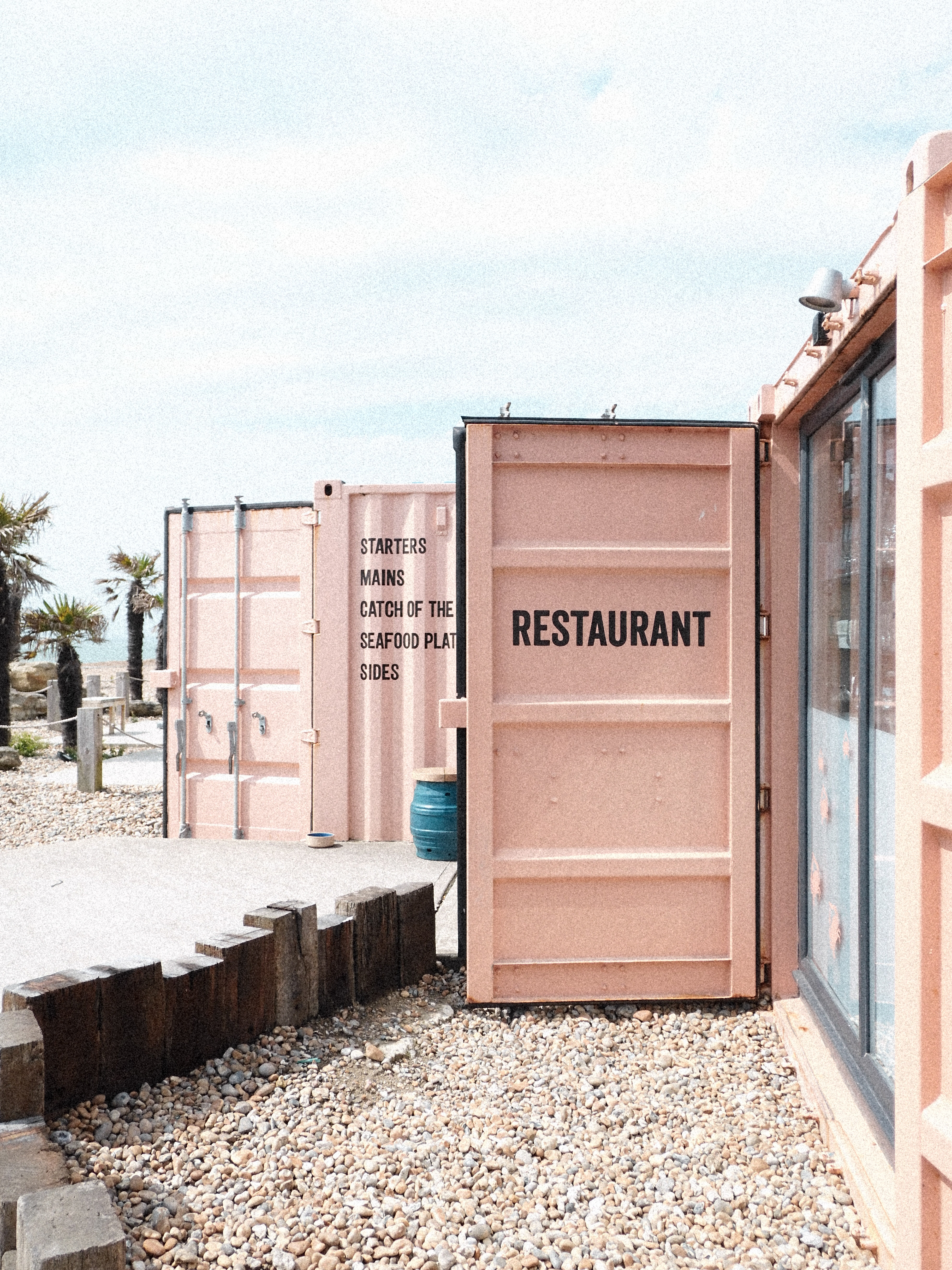 A pink door to a shipping container reading restaurant on a beachfront