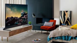 An 8K TV in a bedroom on a low table, with a red chair and bed nearby