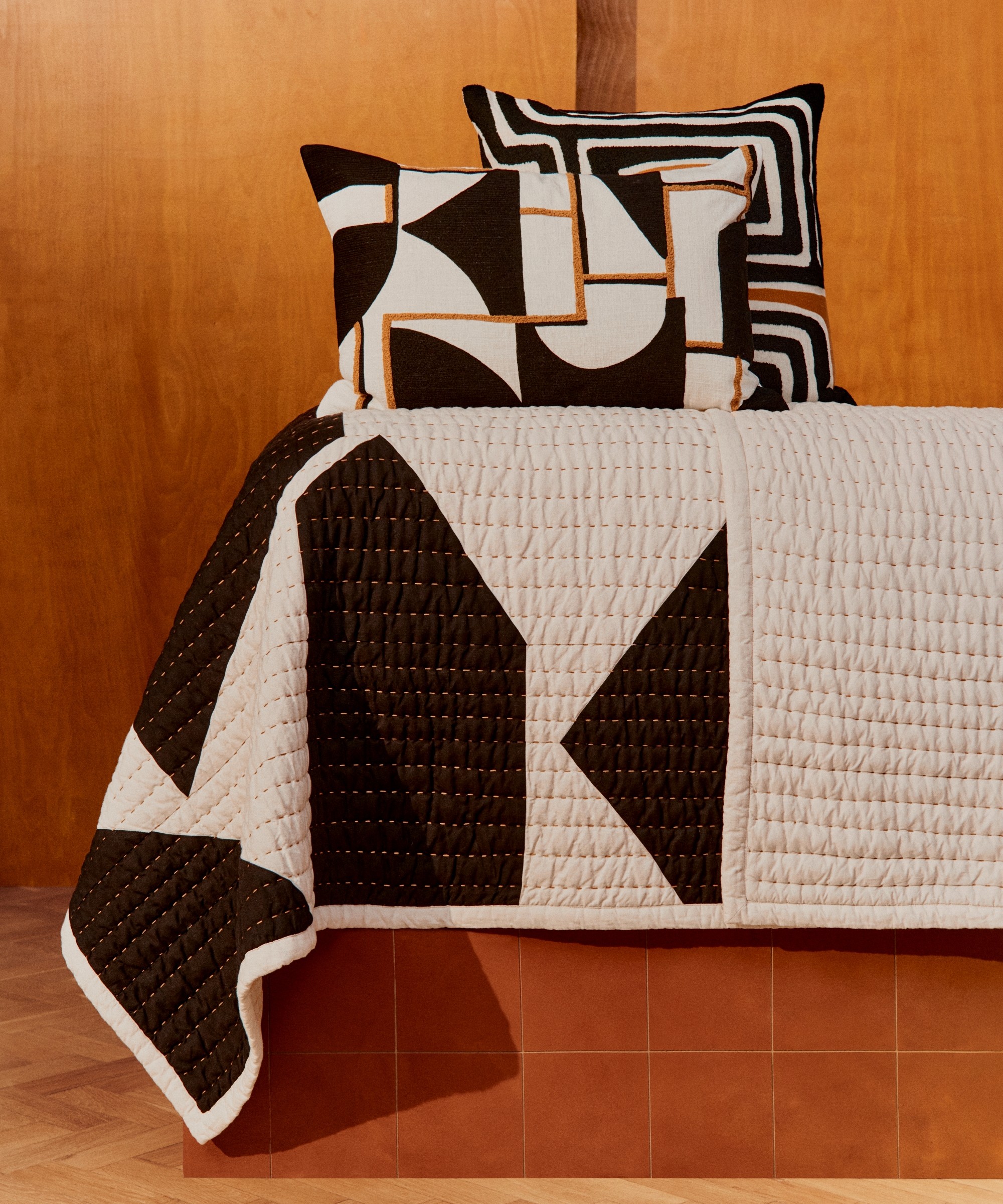 The geometric-pattern quilt and cushions from John Cooper's collection for John Lewis laid out on a tiled stand