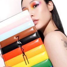A woman with a rainbow eye makeup look holding a makeup palette.