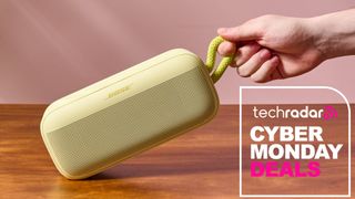 Person holding Bose Bluetooth speaker by carry strap with words 'TechRadar: Cyber Monday deals'
