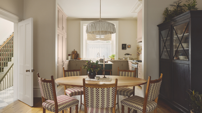 a kitchen and dining room with a table with five chairs, a black cabinet to the right, and a small kitchen in the background