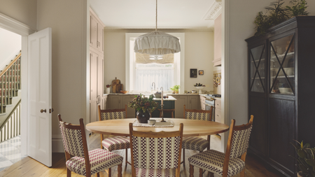 a kitchen and dining room with a table with five chairs, a black cabinet to the right, and a small kitchen in the background