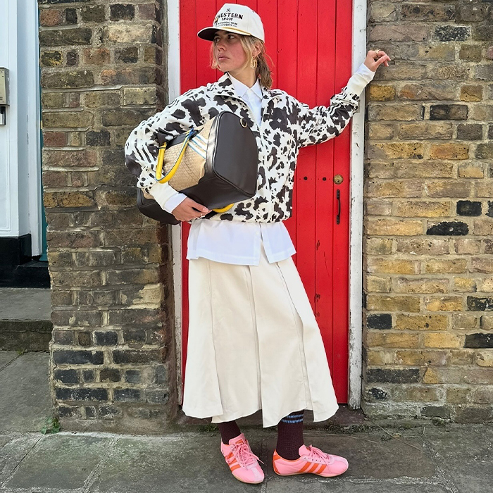 torivan wears white skirt and pink sneakers, and a cow print jacket while posing 