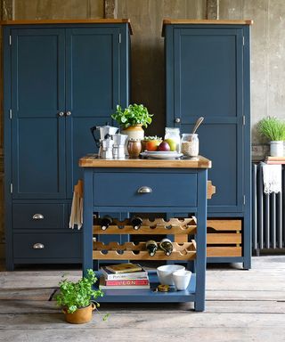 A dark blue butcher's block with built-in wine rack, books underneath it, and a tall blue cabinet behind it