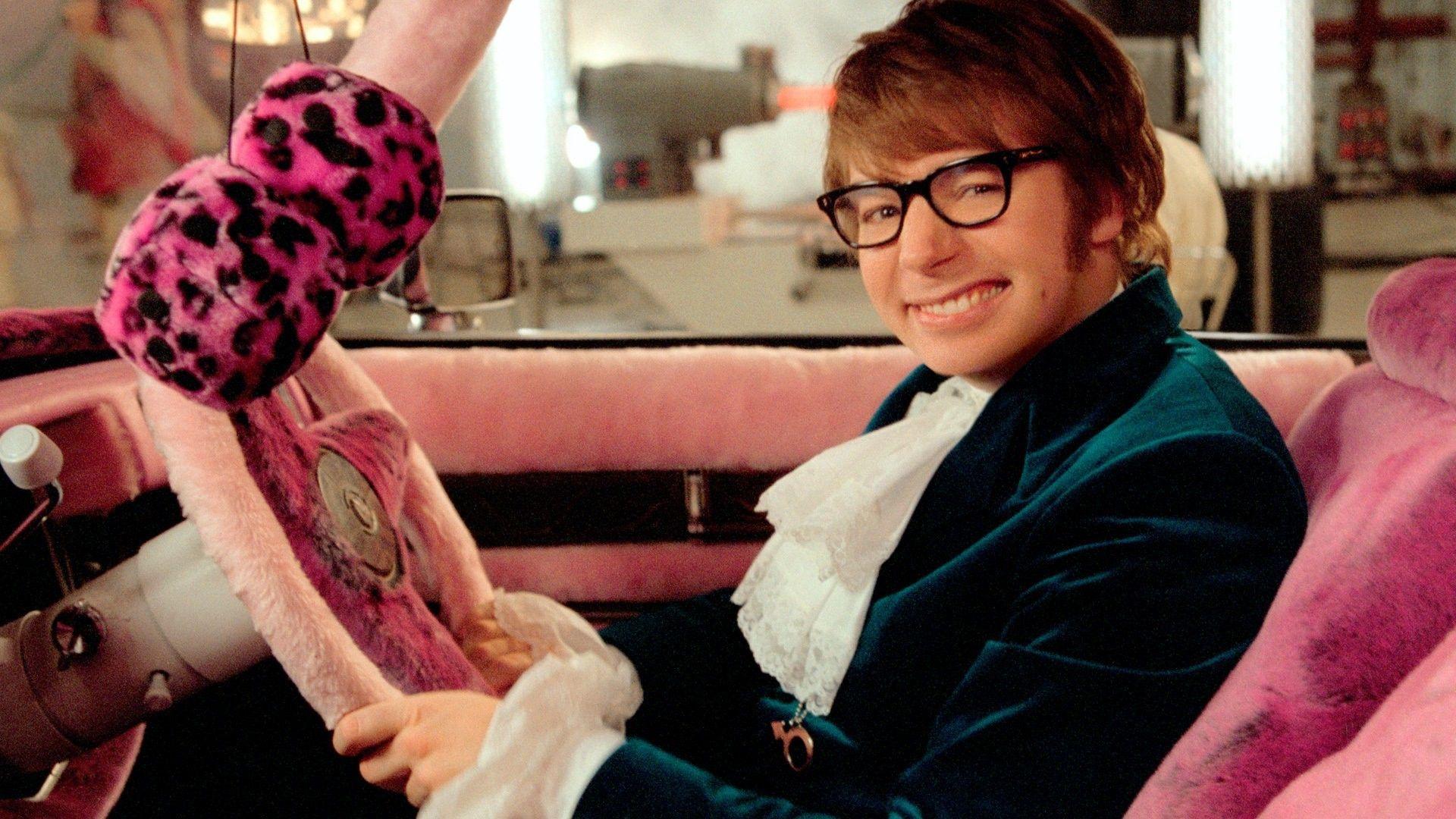Austin Powers smirks as he sits at the wheel of a pink car