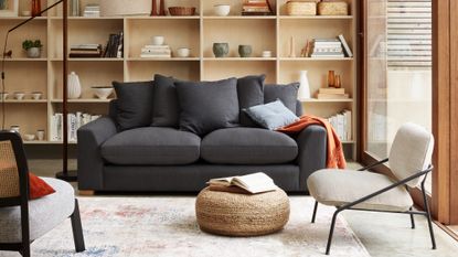 dark grey sofa in front of pale wood open shelves and a rattan pouffe