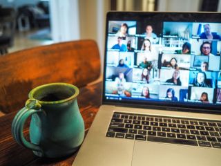 Laptop computer next to mug of coffee displays Zoom videoconference. 