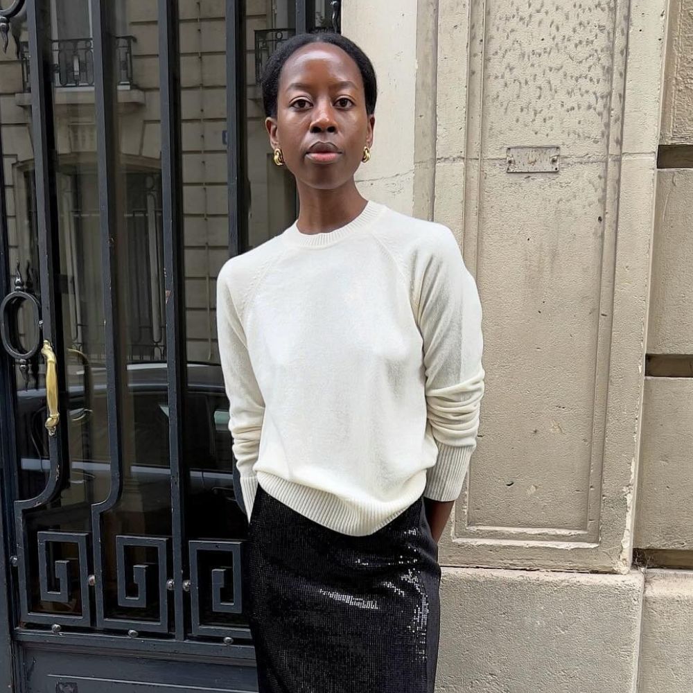 Influencer @sylviemus_ stands outside in Paris wearing a cream fine-knit jumper with a black sequinned pencil skirt and pointed-toe heels.