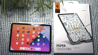 An iPad tablet with a PaperTouch Pro screen protector sitting next to the screen protector packaging.