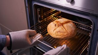 Someone removing a loaf of bread from the oven while wearing oven mitts