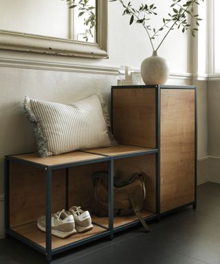 An entryway with a wooden shelving unit with a striped throw pillow, a vase with branches, trainers, and a bag on it