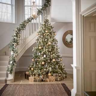 An artificial Christmas tree in a grand entranceway with sweeping staircase