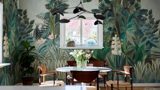 A wall covered in Rebel Walls' The Equatorial Jungle by Rousseau Wallpaper with a table and chair sat in front of it