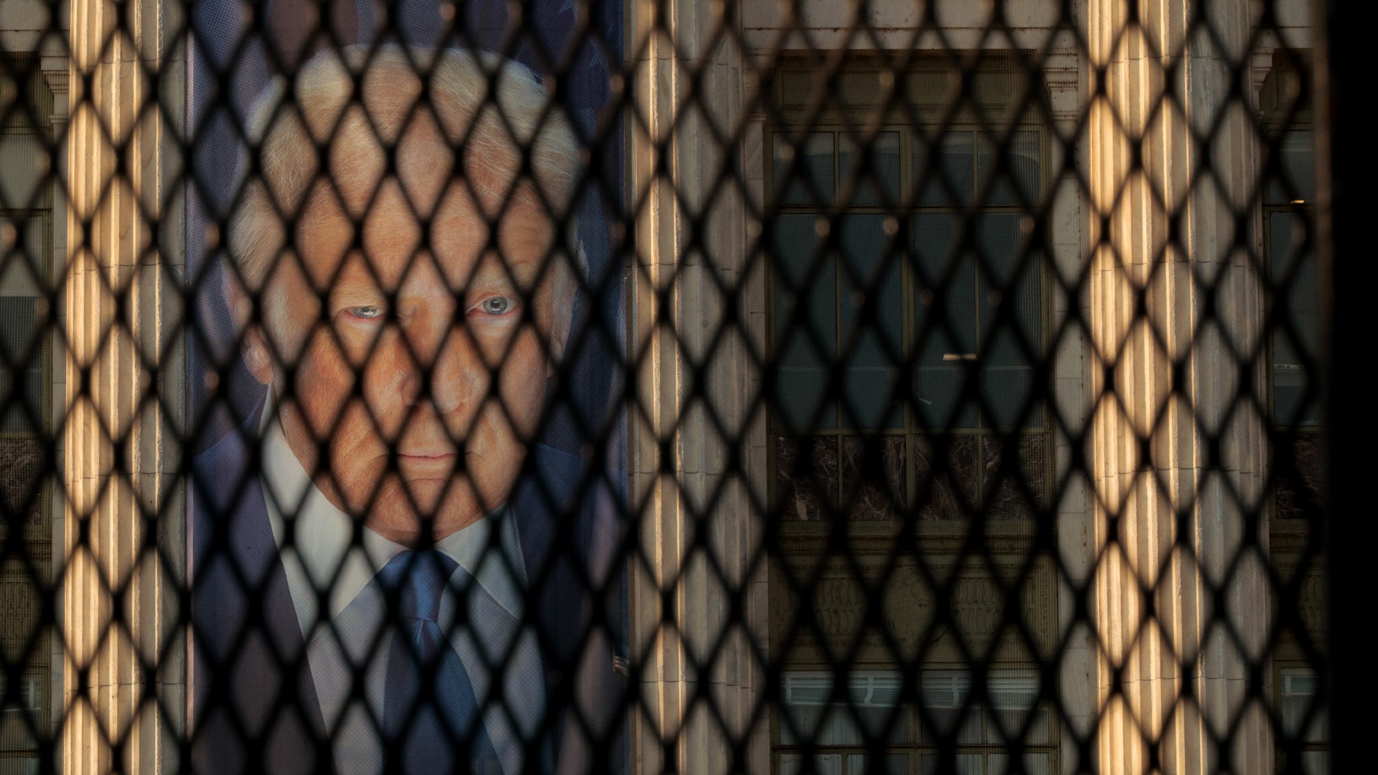 A banner with the image of Donald Trump seen through security fencing 