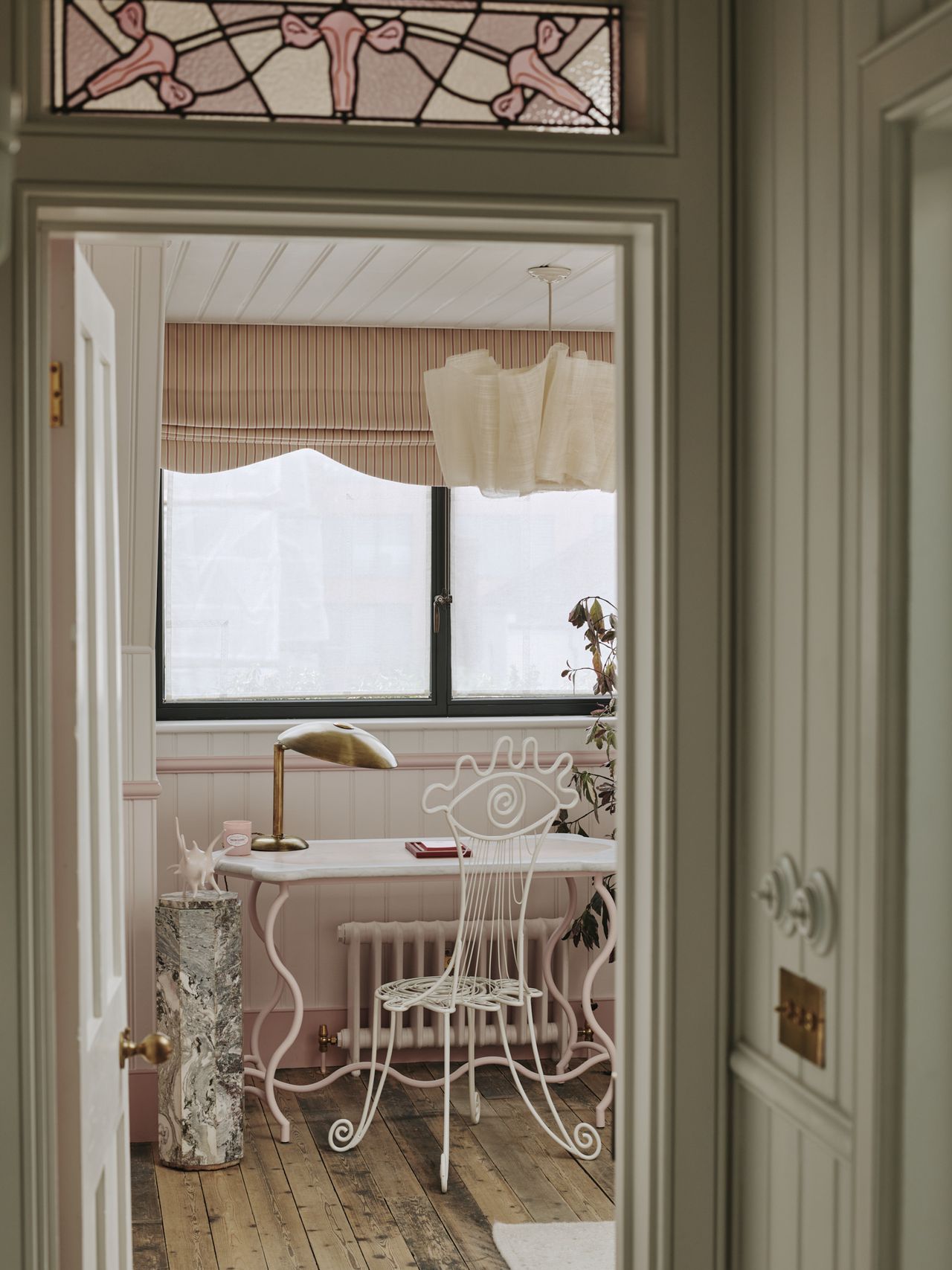 Whimsical pink desk with a wrought iron chair in a doodled eye shape and marble pedestal with spiky pink sculpture on top.