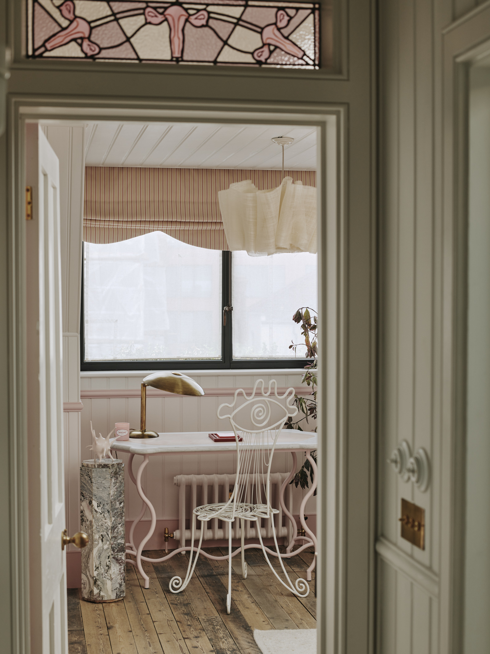 Whimsical pink desk with a wrought iron chair in a doodled eye shape and marble pedestal with spiky pink sculpture on top.