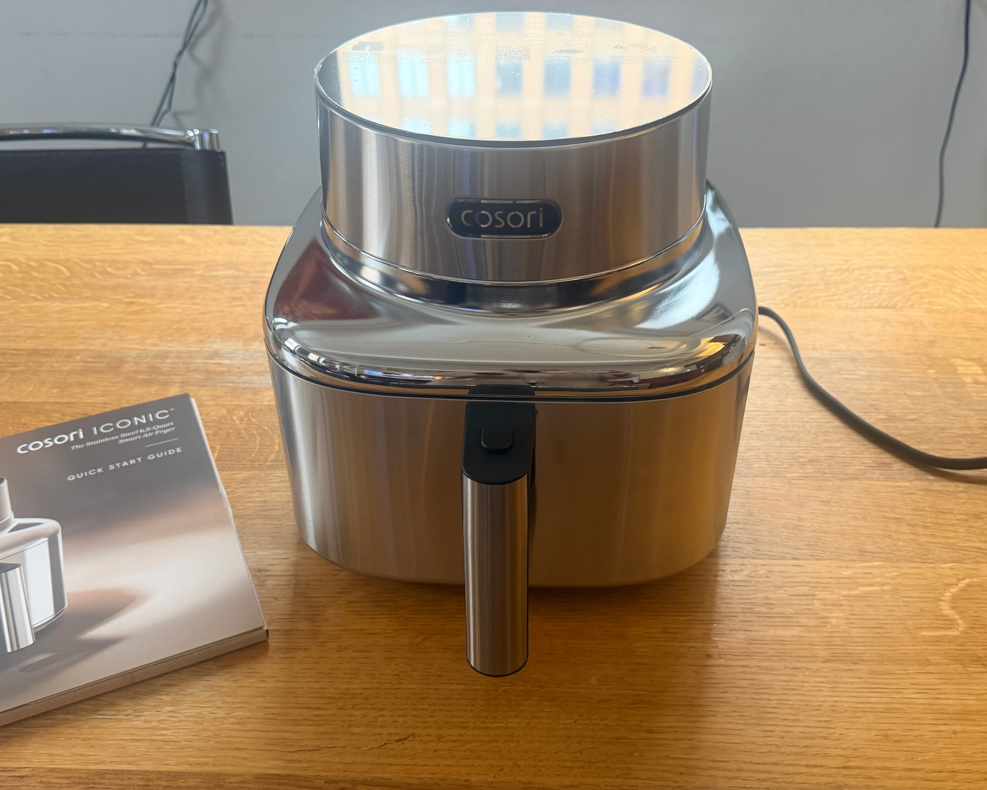 Silver air fryer sitting on a wooden table with an instruction manual next to it