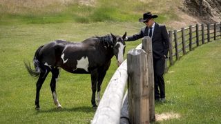 John Dutton in a black suit with a matching black and white horse