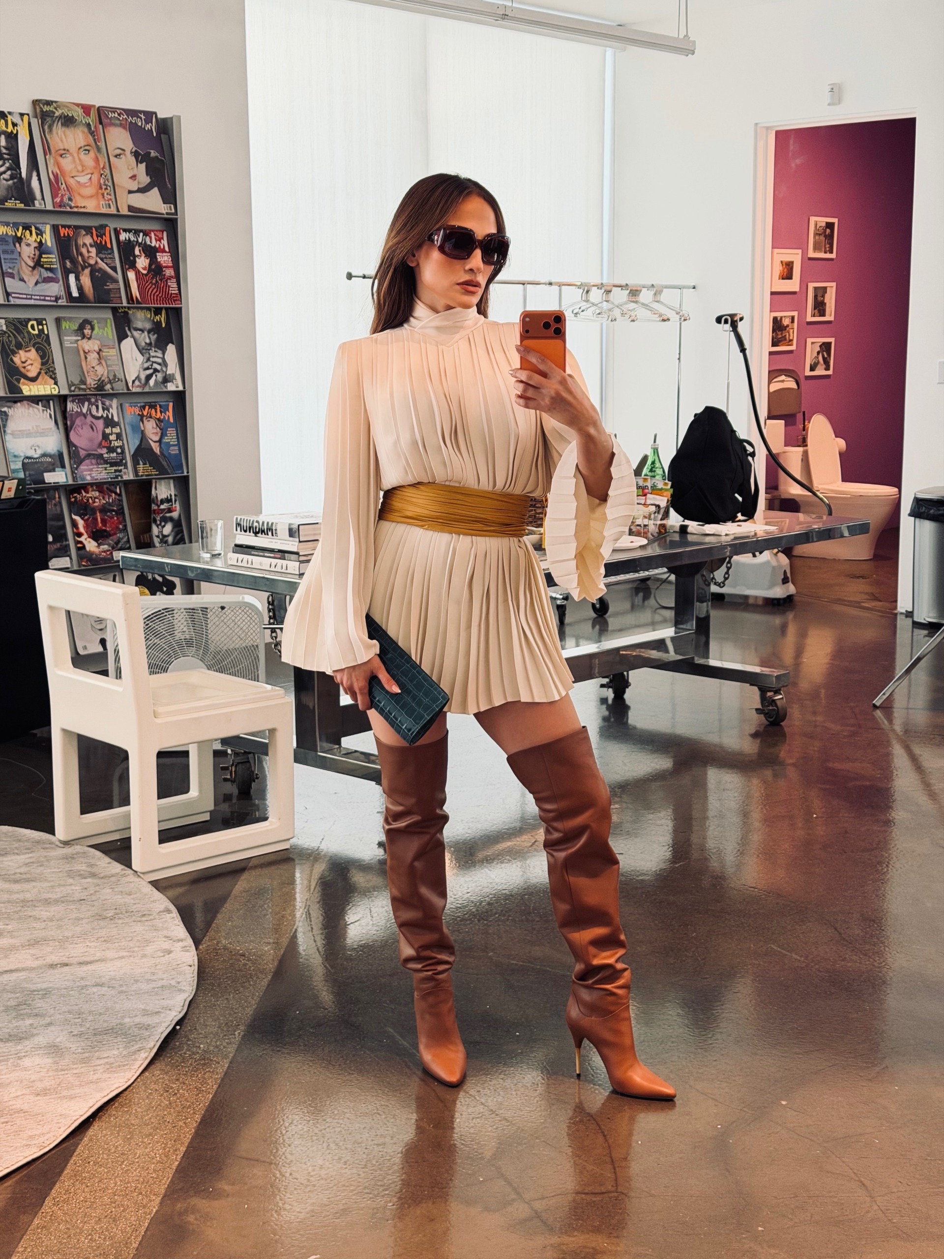 jennifer lopez wears a pleated minidress, tan thigh high boots, and a clutch.