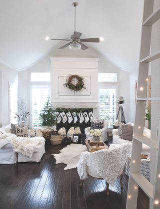 white living room with Christmas decorations, stockings on fireplace, small tree, wreath, wooden floor, knitted throws