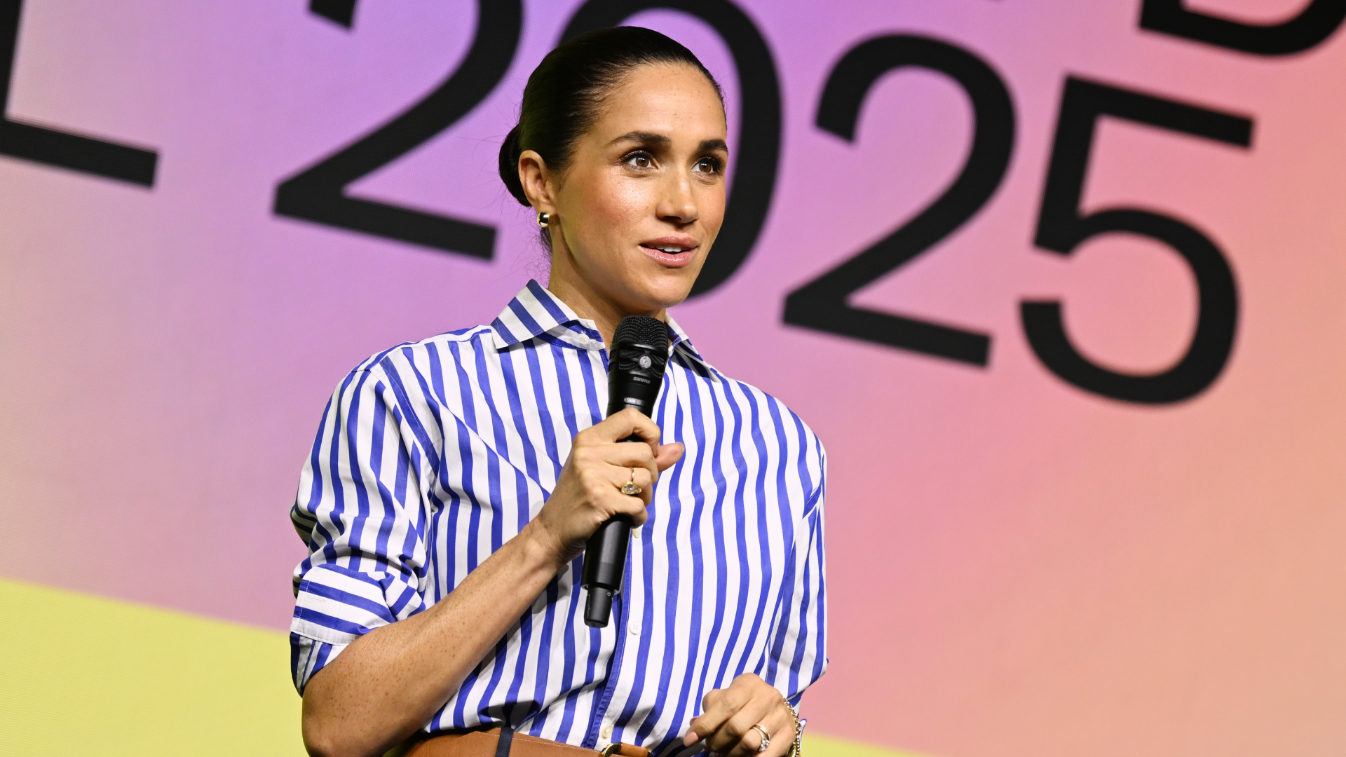 Meghan Markle wearing a blue and white striped top speaking in a mic